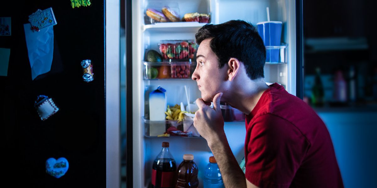 Un joven frente a un refrigerador tratando de elegir algo para comer