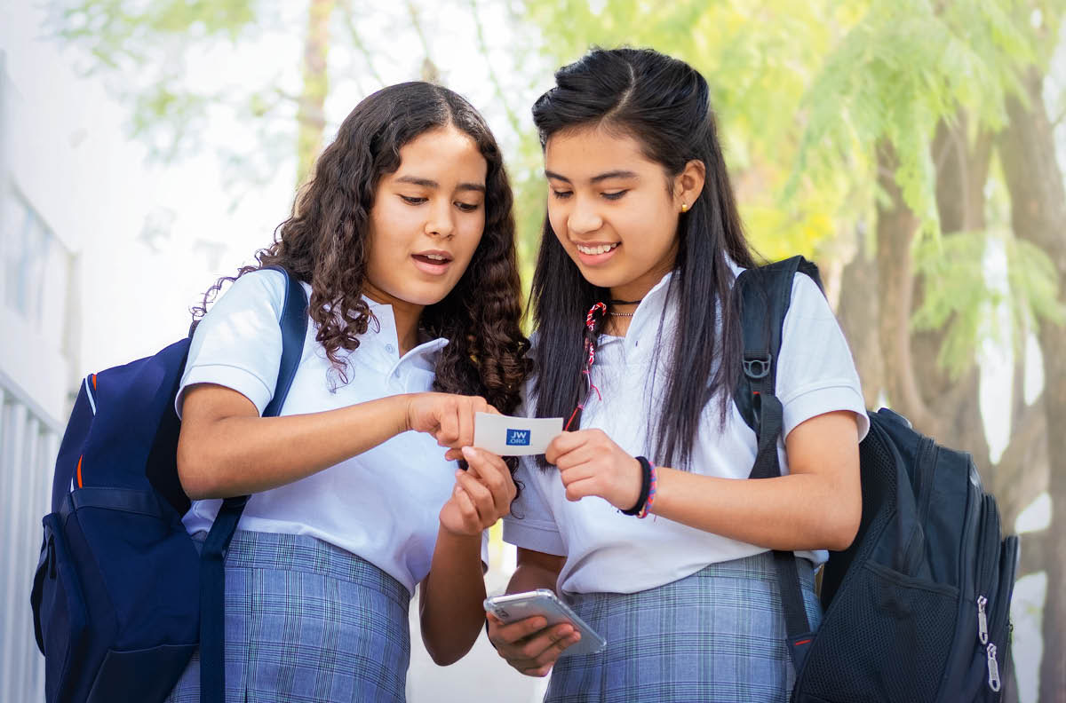 La misma adolescente le da una tarjeta de contacto de jw.org a una compañera de clase.