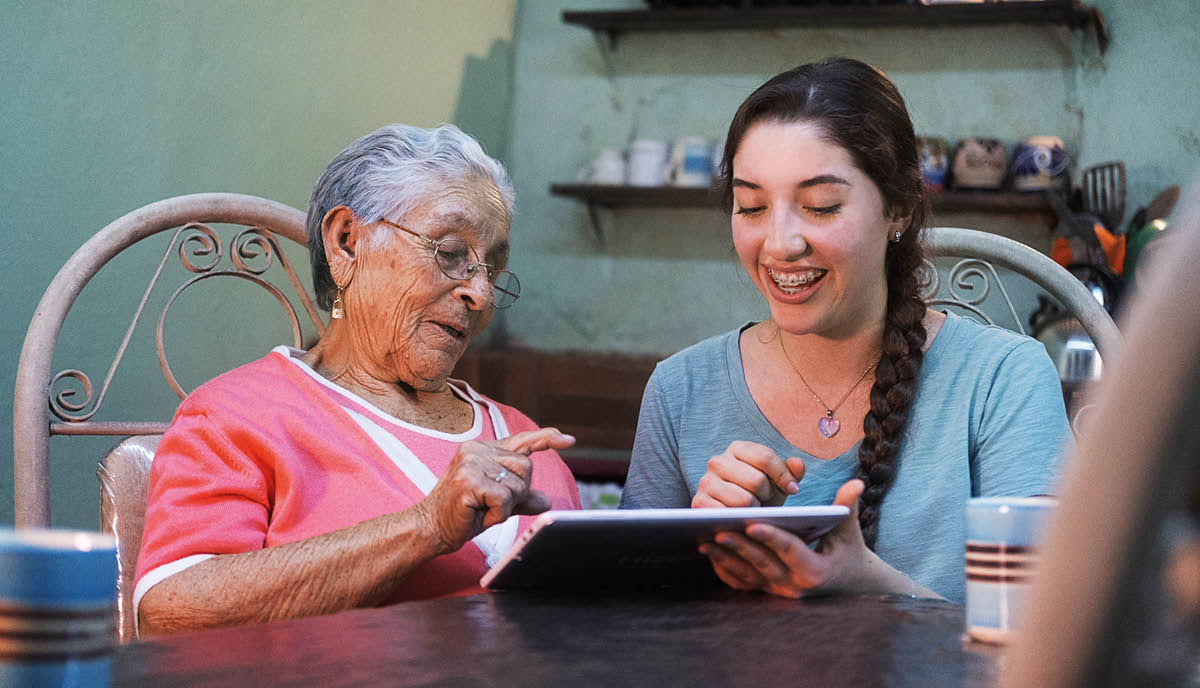 Una joven ayudando a una señora mayor a usar una tablet.