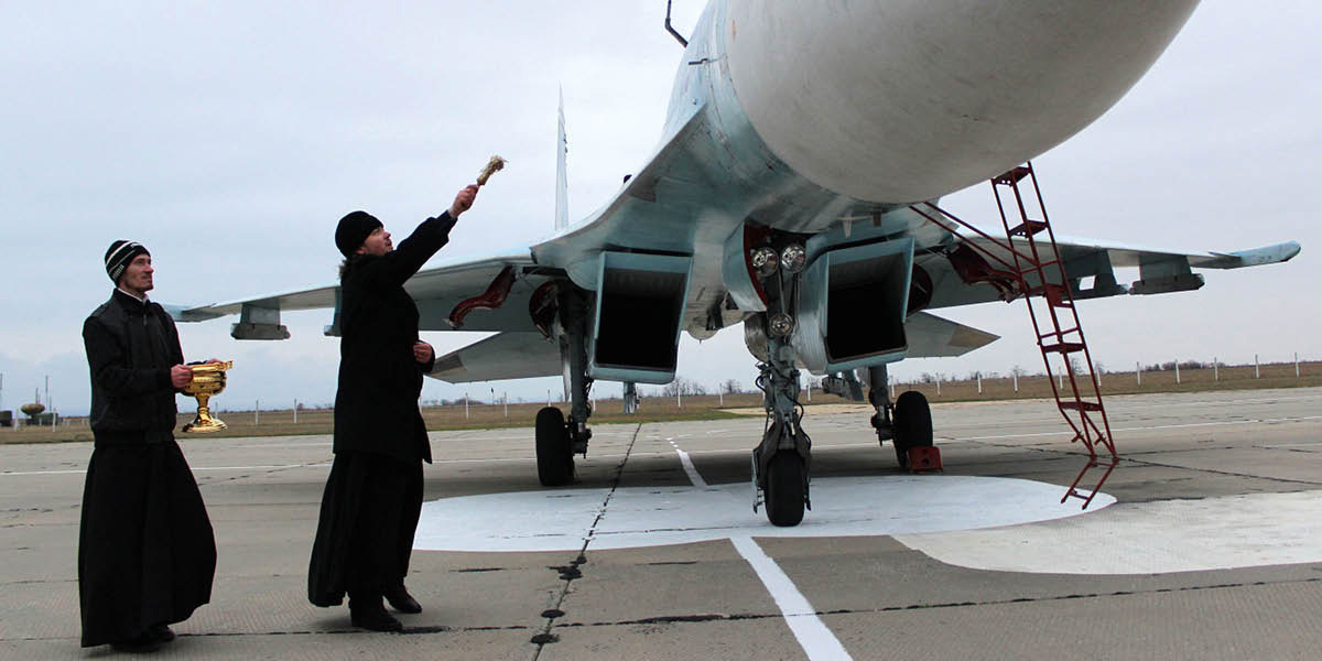 Un sacerdote bendice un avión de combate echándole agua bendita.