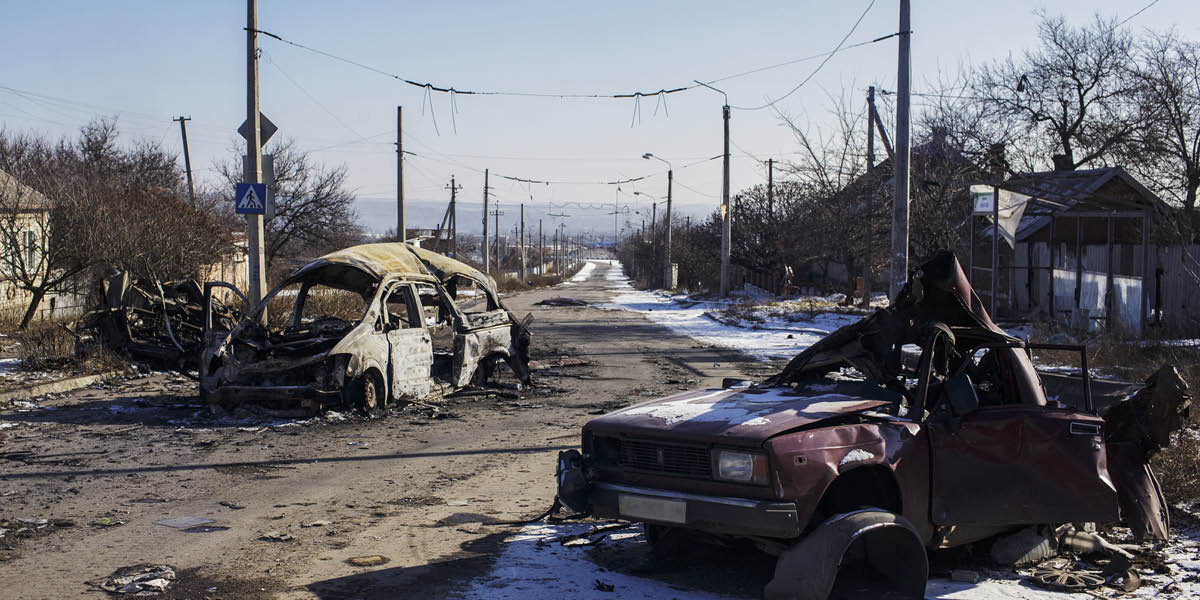 cnt_01: Una calle abandonada en un pueblo de Ucrania devastado por la guerra; se ven algunos vehículos destruidos por las bombas.
