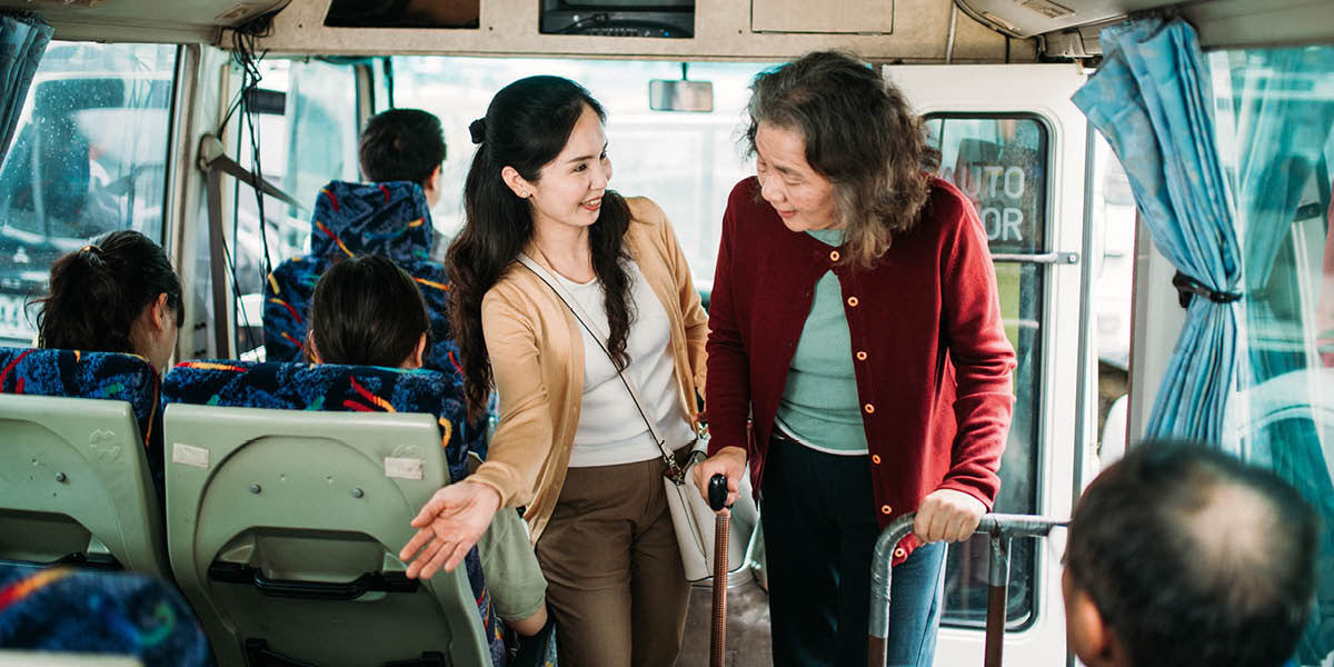 Una mujer le cede su asiento en el autobús a una señora mayor.