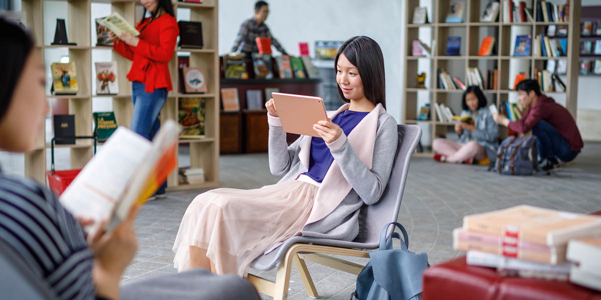 En una biblioteca, una mujer lee la Biblia en su tablet.