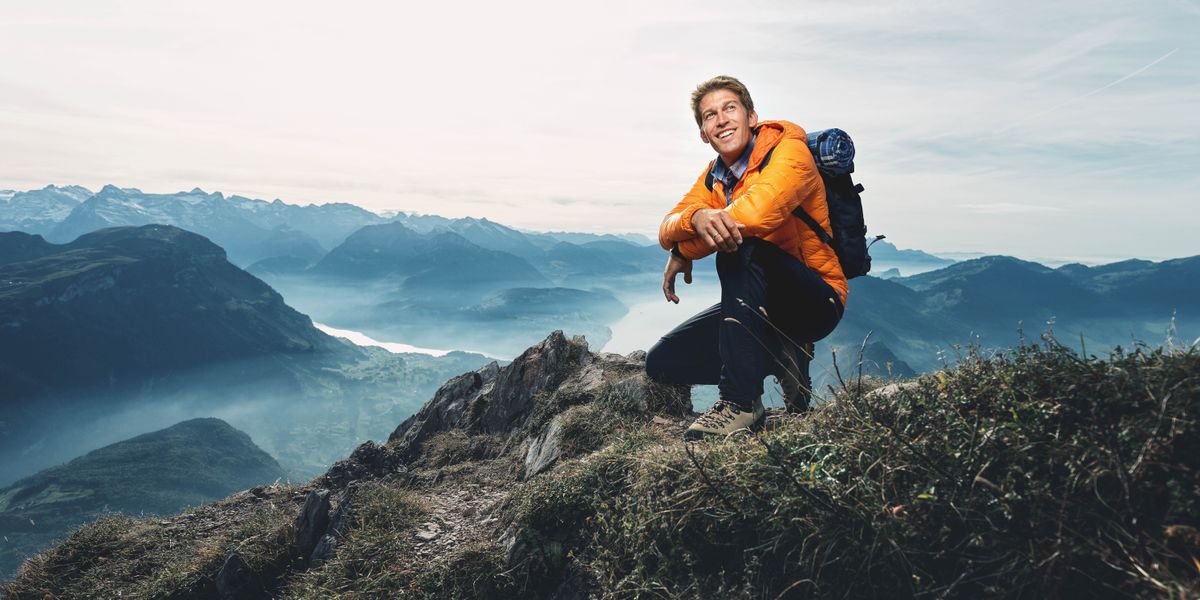 El hombre joven de los artículos anteriores mira a lo lejos con alegría después de alcanzar la cima de la montaña.
