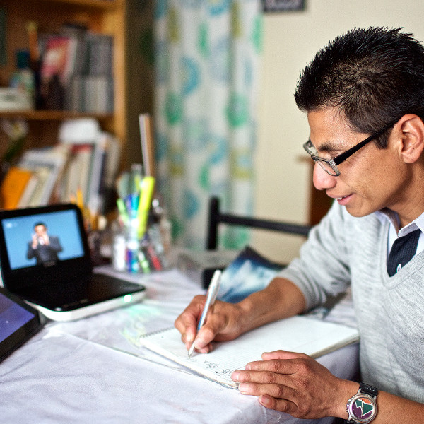 A deaf man named Daniel makes notes as a Mexican Sign Language DVD plays in the background