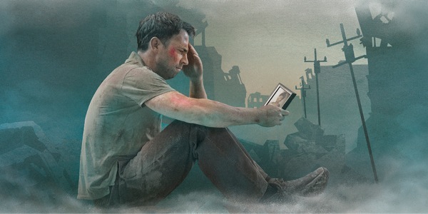 A troubled man looks at a photo while sitting in wreckage