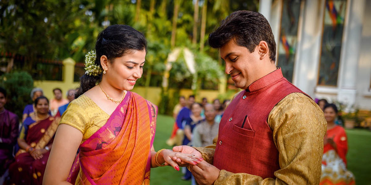 A bride and groom getting married at an outdoor location. The groom places a ring on the bride’s finger.