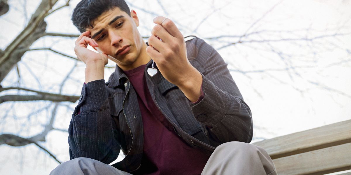 An emotionally distraught young man holds a heart-shaped necklace