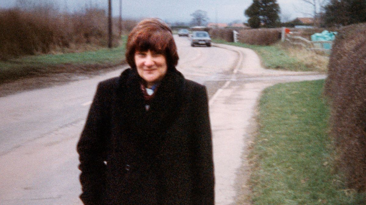 Carol smiling as she walks on a sidewalk.