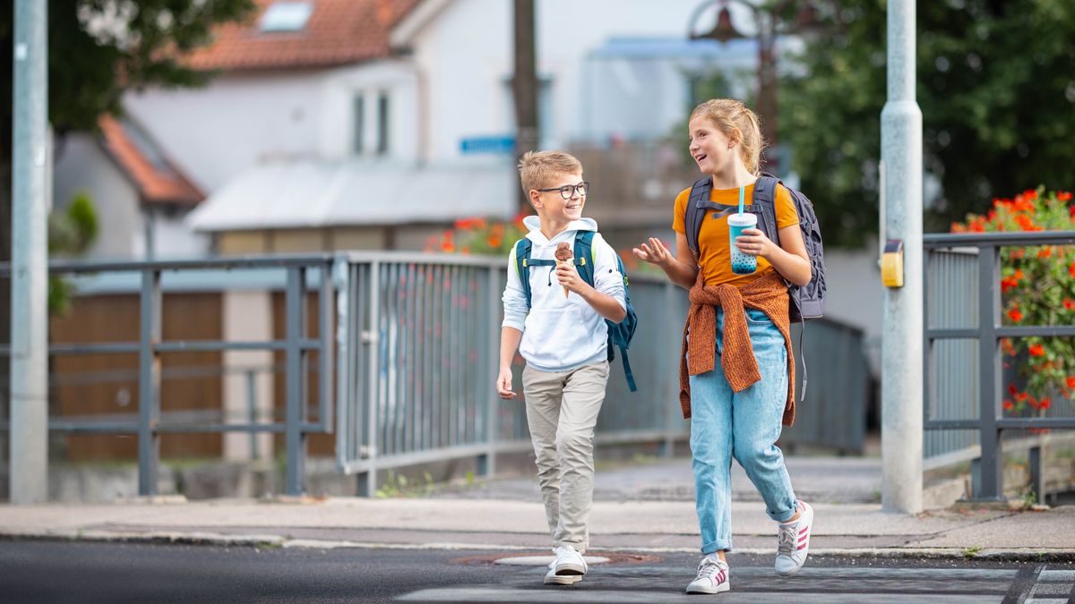 The young sister and her brother happily talk as they walk and enjoy some cold refreshments.