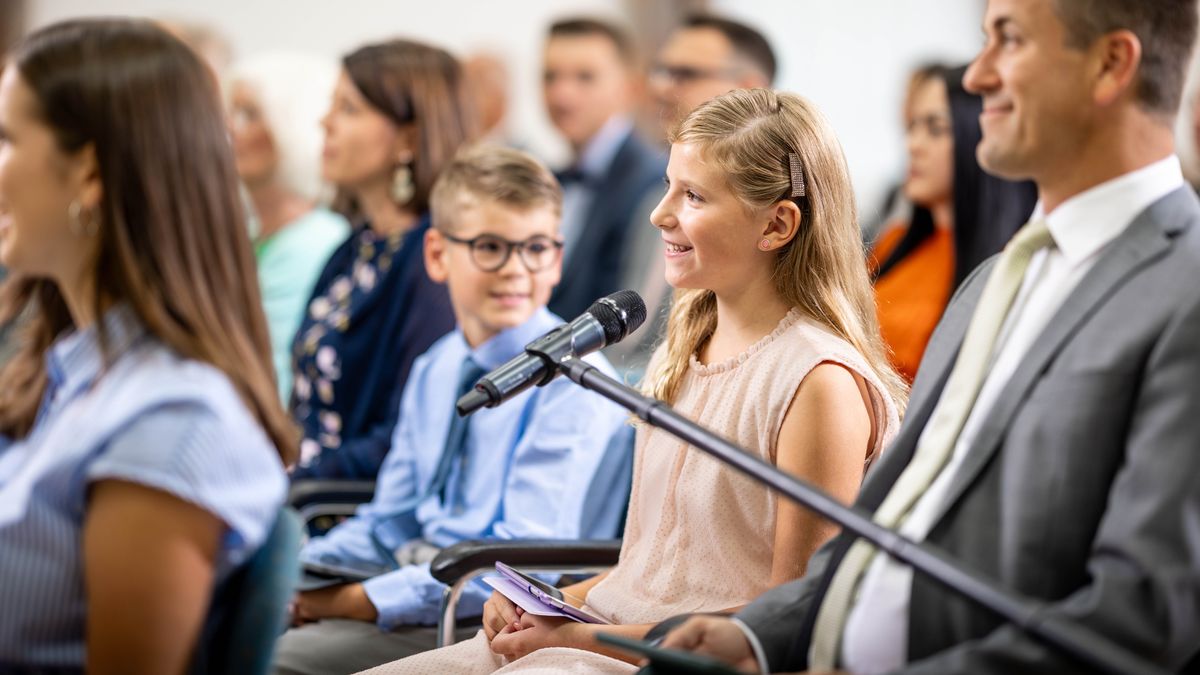 The young sister comments at a meeting as her brother looks over at her with a smile.