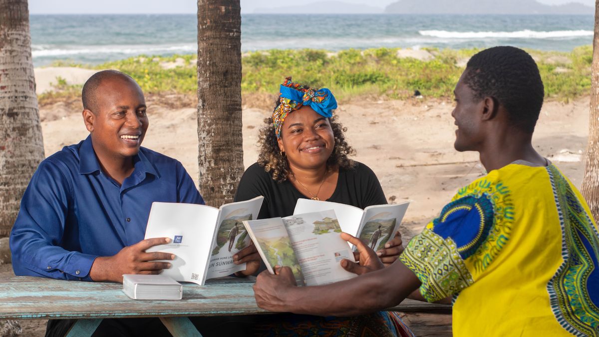 En la playa, un matrimonio le da una clase de la Biblia a un hombre usando el libro “Disfrute de la vida”.