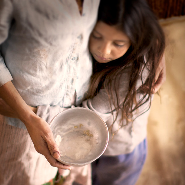 Una mujer abraza a su hija pequeña con un plato vacío en las manos