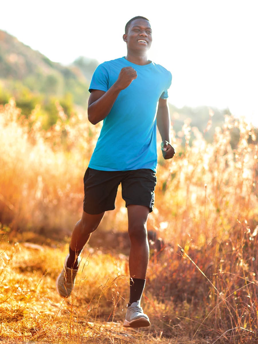Un jeune homme fait du jogging à l’extérieur avec un large sourire.