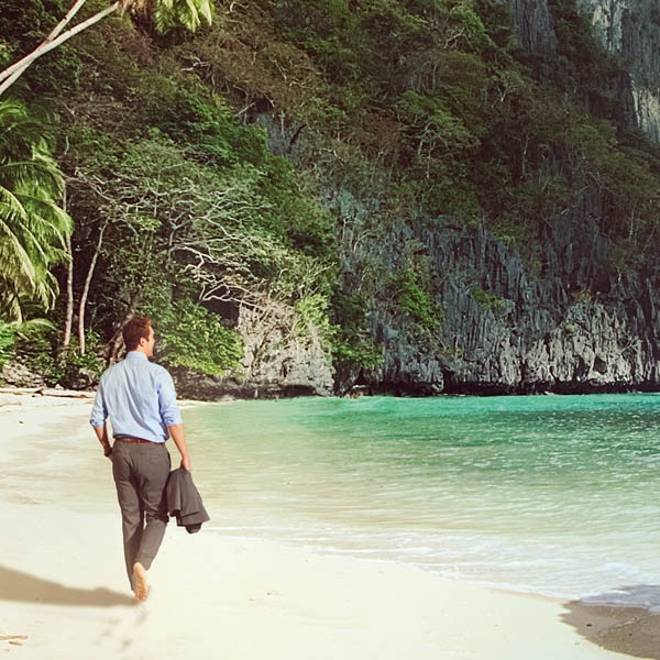 Un homme en costume marche le long d’une plage pieds nus tout en admirant l’océan.