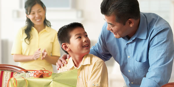 Des parents discutent avec leur jeune garçon pendant qu’il déballe un cadeau.
