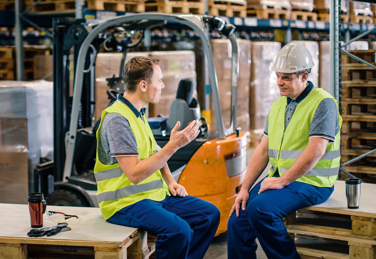 Un frère donne à un membre de sa famille non Témoin une invitation au Mémorial. Ils sont dans une cuisine, assis à table. En arrière-plan, on voit leurs femmes discuter tout en préparant le repas.