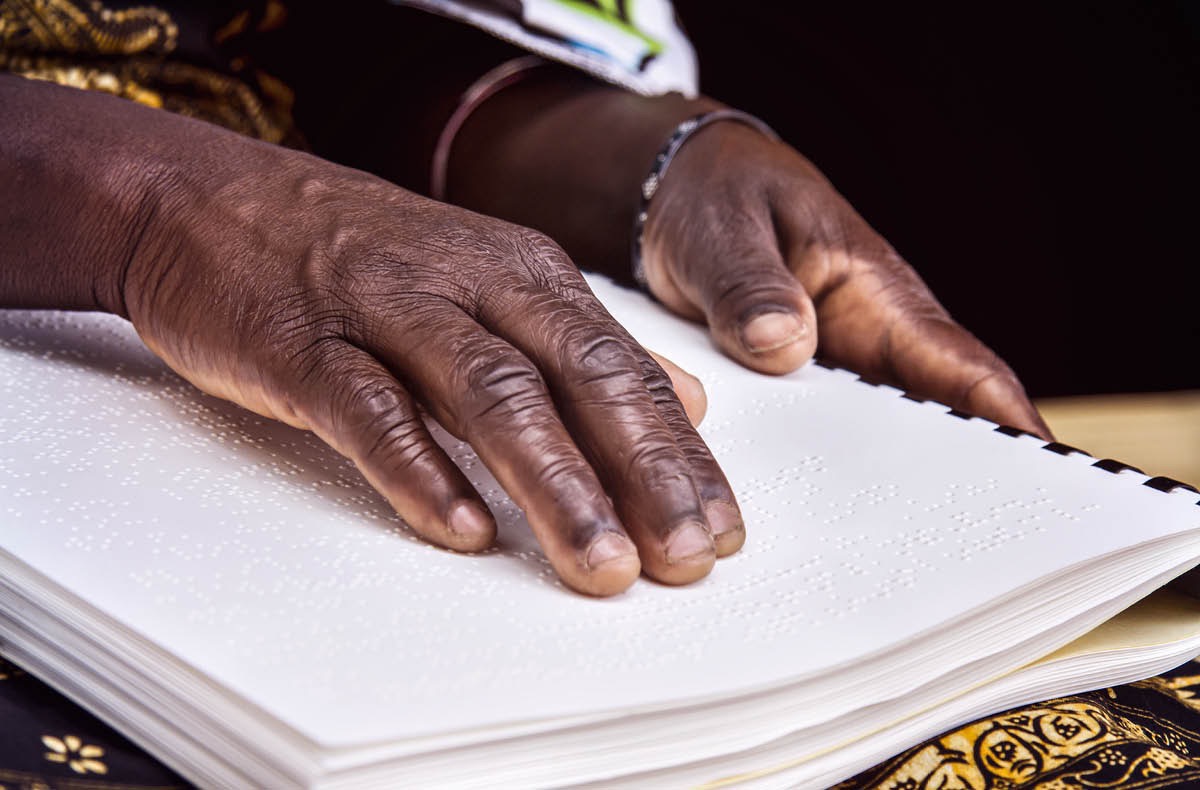 Une sœur aveugle en train de lire en faisant passer ses doigts sur une publication en braille.