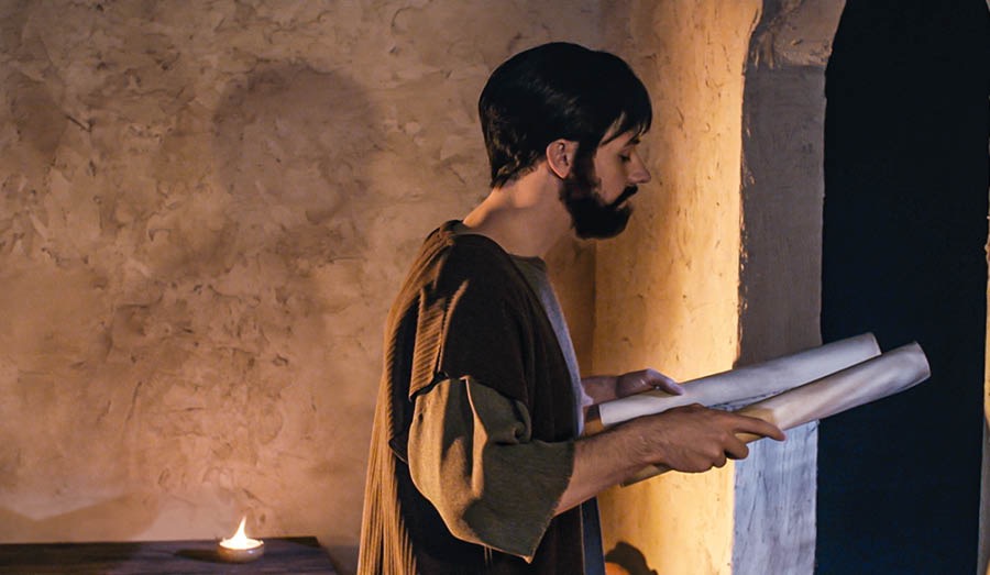 Tard le soir, Timothée, se tenant debout devant une fenêtre, lit un rouleau.