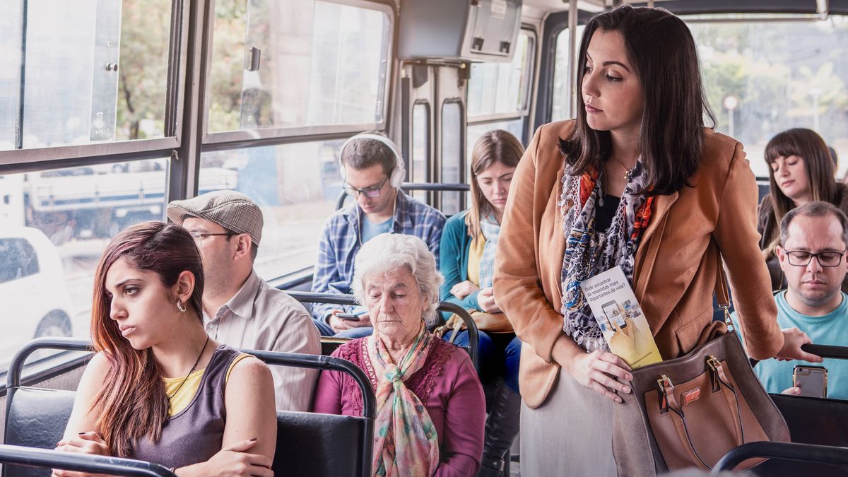 Dans un bus, une sœur observe une jeune femme qui semble soucieuse. La sœur a dans la main le tract « Où trouver les réponses aux grandes questions de la vie ? »