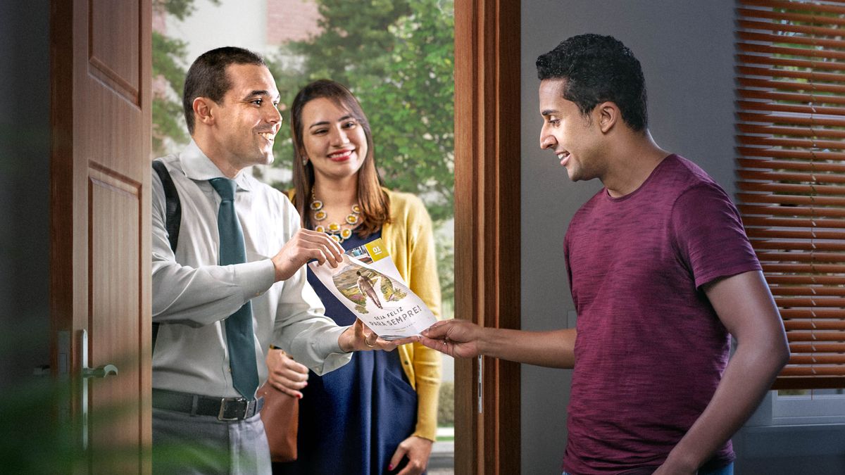 Un couple qui prêche de porte en porte propose à un homme la brochure « Vivez pour toujours ! ».