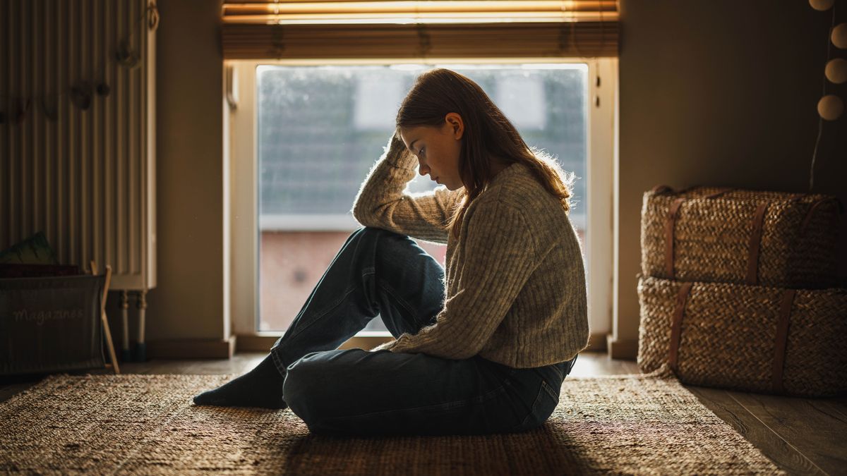 Seule dans sa chambre, une adolescente en proie à une angoisse profonde regarde le sol fixement.