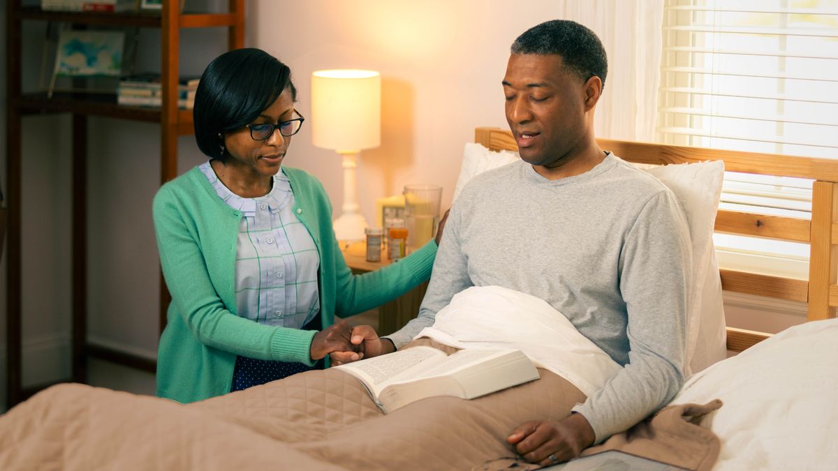 Un frère malade est assis dans son lit et prie avec sa femme.