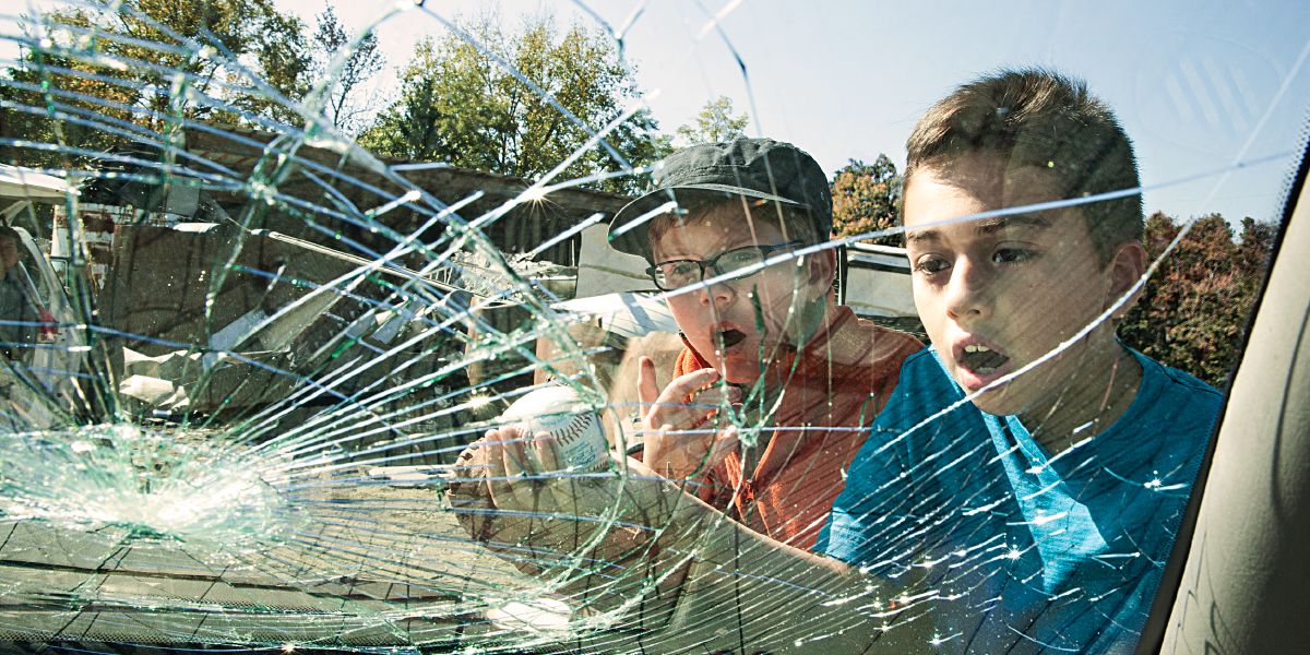 Deux garçons regardent la vitre cassée d’une voiture