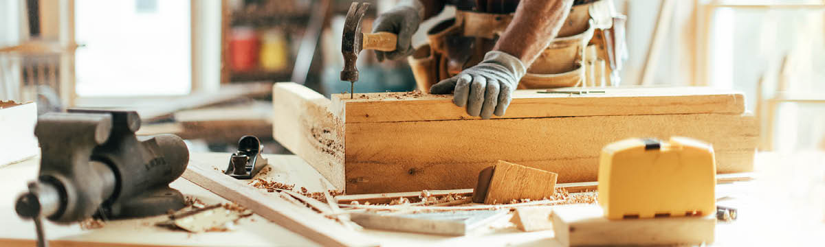 Puuseppä hakkaa vasaralla naulaa puuhun.