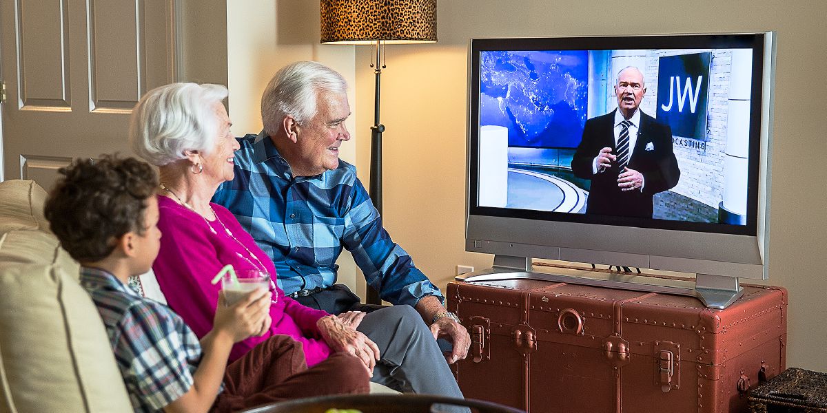 Iäkäs pariskunta ja pikkupoika katsovat ohjelmaa JW Broadcastingista.