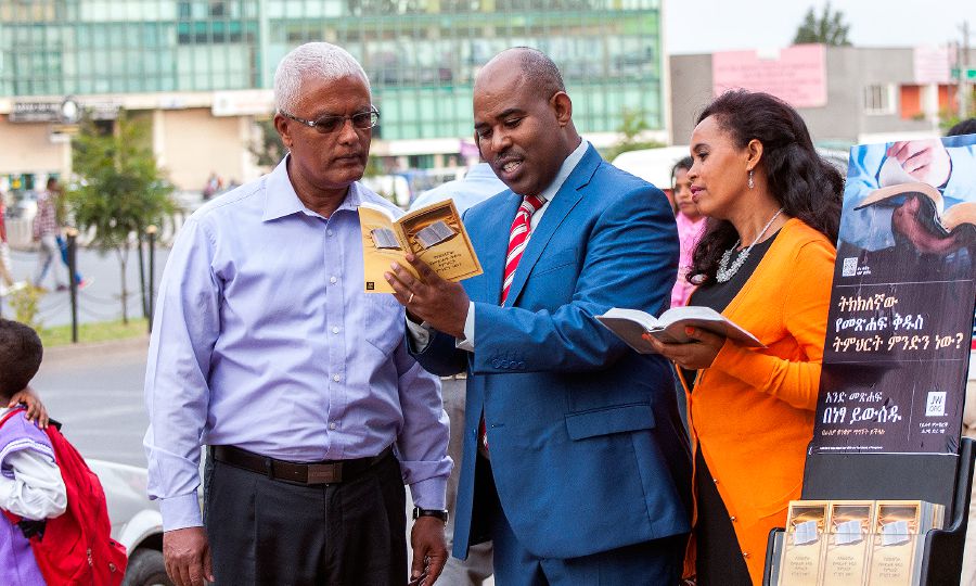 Jehovan todistajat saarnaavat miehelle kirjallisuuden esittelykärryn vieressä Addis Abebassa Etiopiassa käyttäen amharankielisiä julkaisuja.