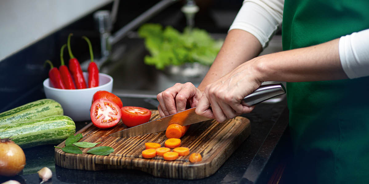 Une femme découpe des légumes frais sur une planche à découper en bois.
