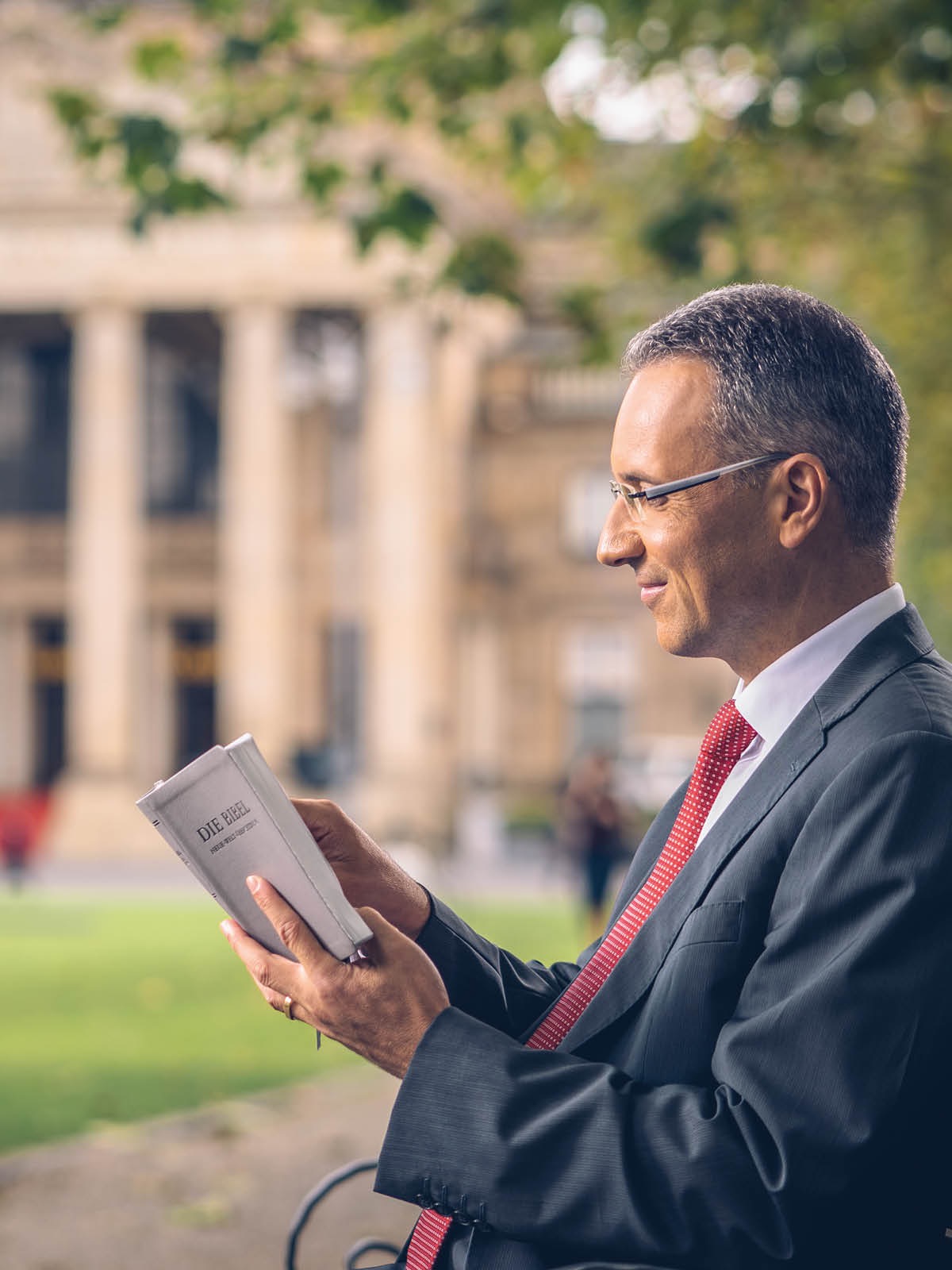 Un home lendo a Biblia sentado nun banco diante dun edificio do goberno.