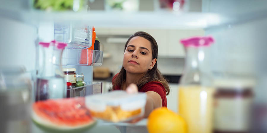 Eine Frau stellt einen Behälter mit Essen in den Kühlschrank.