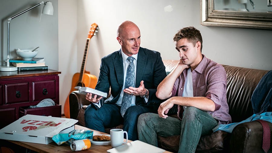 Ein Ältester gibt einem jungen Bruder mit der Bibel in der Hand Rat zum Thema Sauberkeit. Die Wohnung des jungen Bruders ist unordentlich.