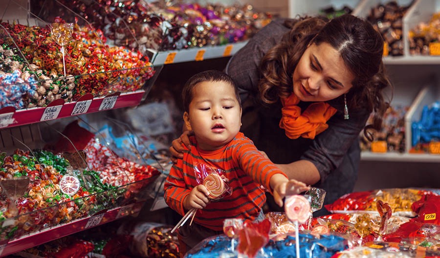 Un niño intentando tomar un caramelo de una tienda y su madre diciéndole que no