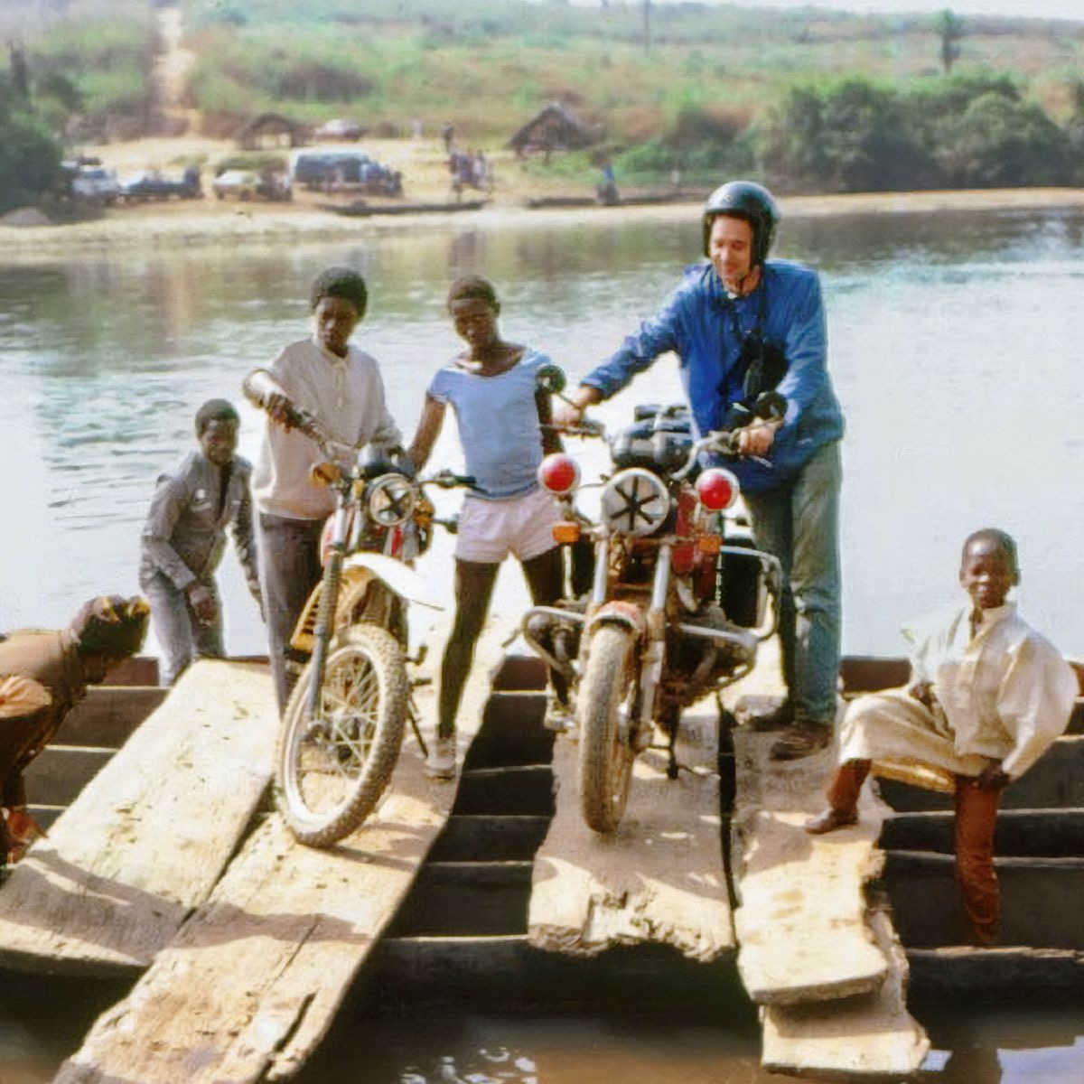 Robert y otras personas con sus motos, cruzando un río en una balsa.