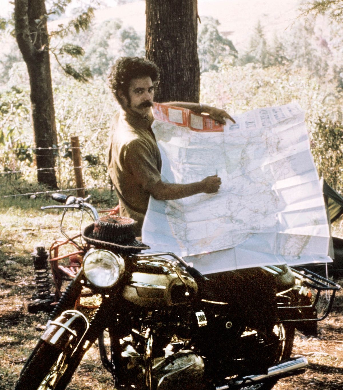 Robert de pie junto a su moto, mostrando un mapa de sus viajes.