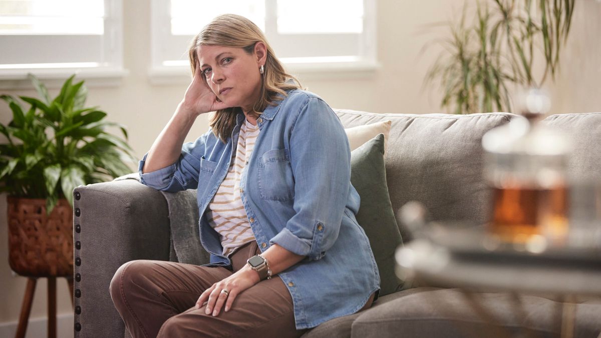 Wata ꞌyarꞌuwa zaune a gida tana kallon kwalbar giyar da ke kusa da ita tana tunani.