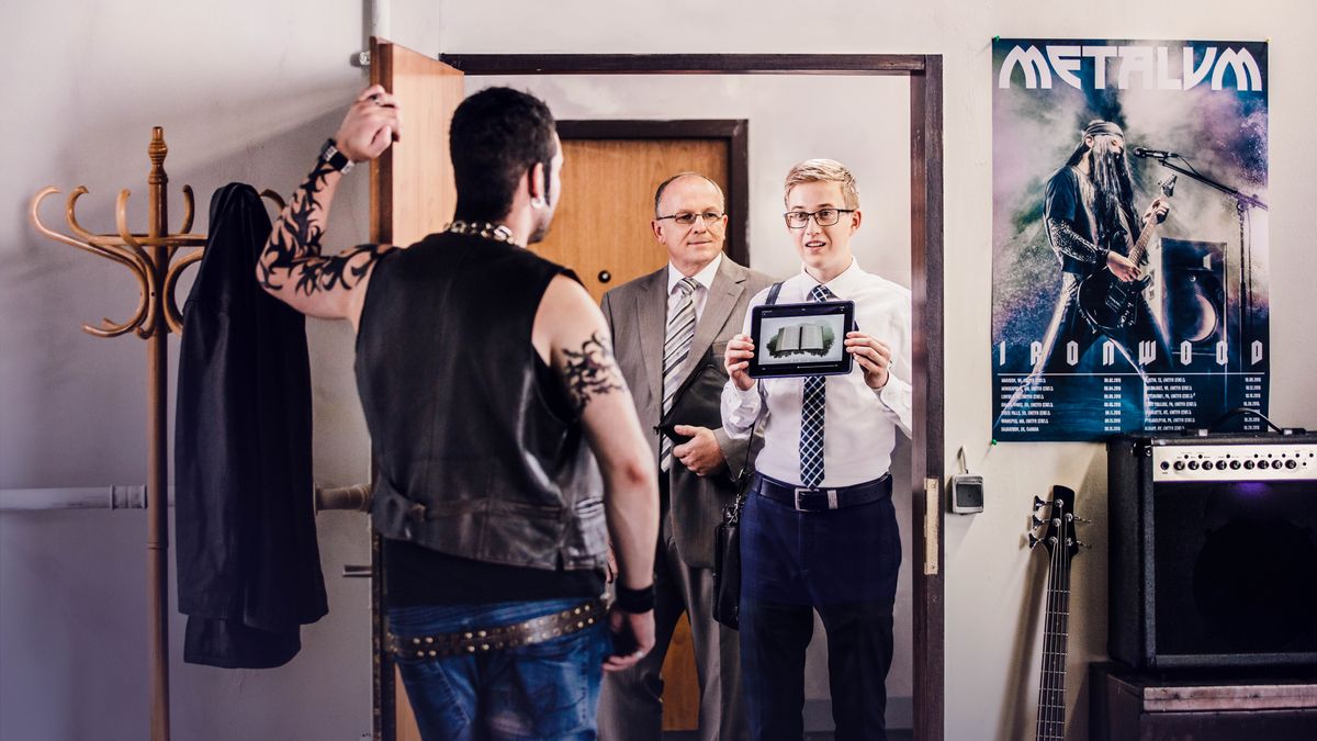 Two braddahs preach to one scary looking guy wit tattoos. Da younga braddah play da video “Study Da Bible, Wat Fo?” Get one poster of a heavy metal band on da guys wall.