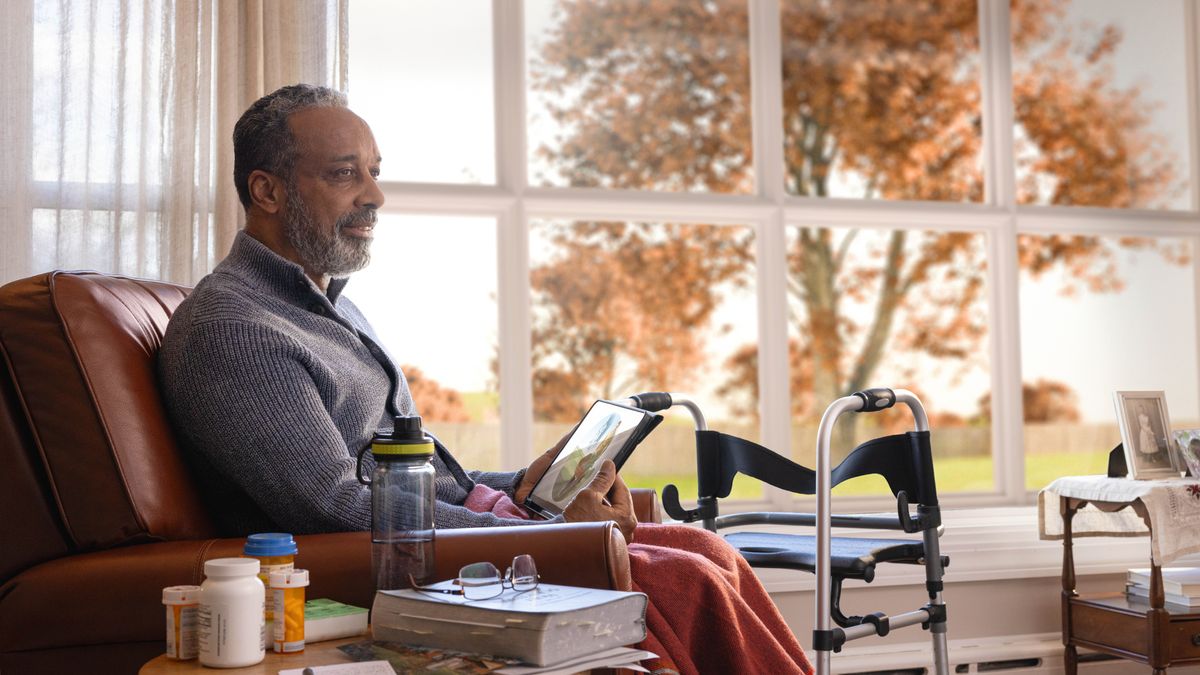 Da olda braddah sitting at home in da fall an tinking about da picha of Paradise on his tablet. He get one walker nex to him an plenny bottles of medicine.