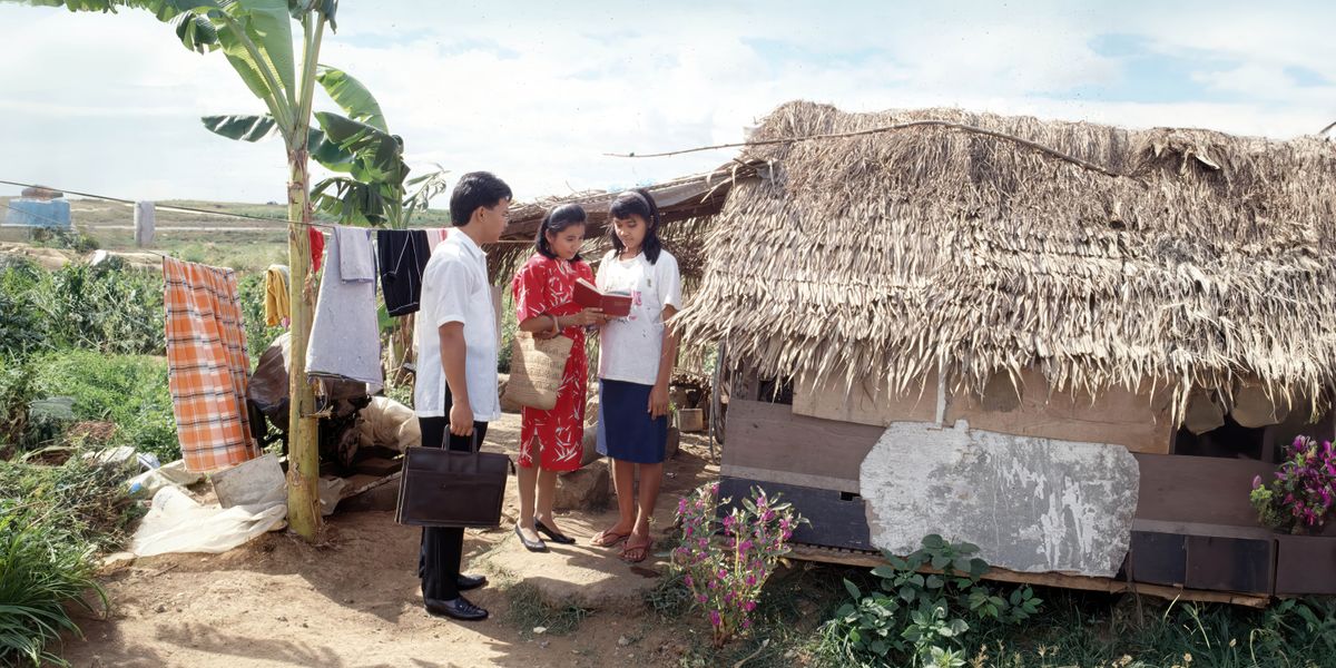 Sepasang suami istri di Filipina mengabar kepada seorang wanita di depan rumahnya yang sangat sederhana.