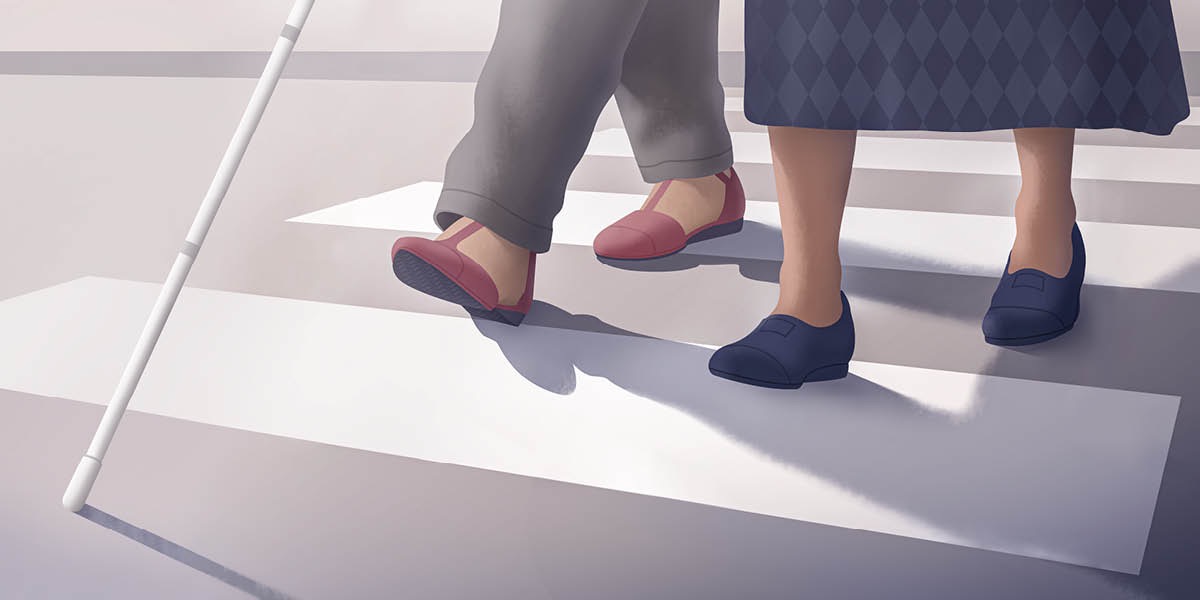 Seorang saudari sedang membantu seorang wanita tunanetra menyeberang jalan. Wanita itu menggunakan tongkat.