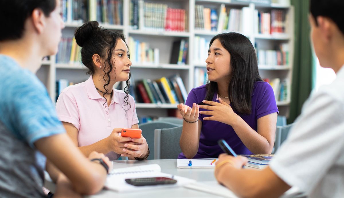La ragazza di prima sta parlando con alcuni compagni nella biblioteca della scuola.