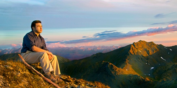 Un uomo seduto sulla vetta di una montagna osserva il paesaggio e il cielo suggestivo