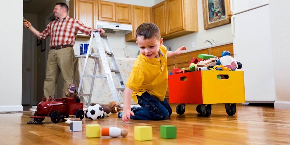 Un bambino mette a posto i giocattoli mentre il padre pittura la parete della cucina