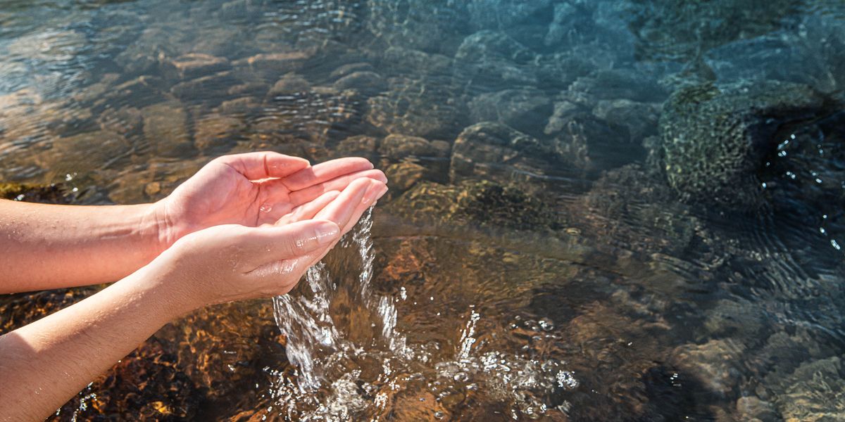 Una donna prende tra le mani un po’ d’acqua pulita da un ruscello.