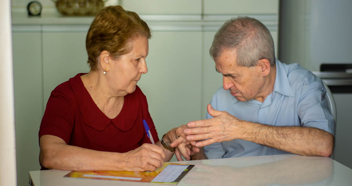 Maria Lúcia scrive una lettera mentre appoggia la mano sinistra sulla mano di José Antônio per seguire quello che lui segna.