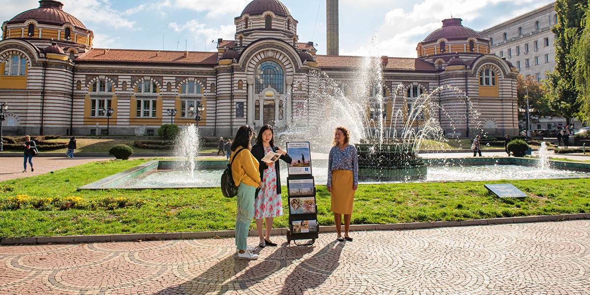 Due sorelle in piedi vicino a un espositore mobile predicano a una donna.