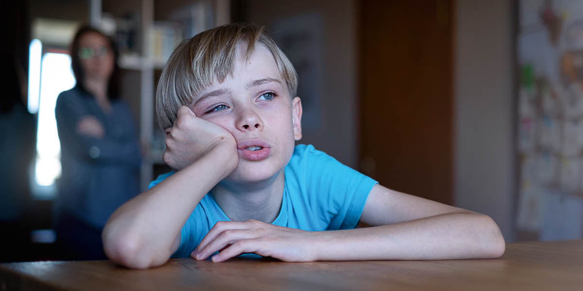 Una madre vede suo figlio seduto a un tavolo che guarda fuori annoiato.